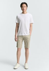 Weißes Baumwoll-T-Shirt, kombiniert mit beigen Shorts, die einen geraden Schnitt und umgeschlagene Säume aufweisen, ergänzt durch weiße Sneakers.