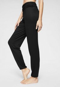 Zwarte stretchy broek met een geplooide tailleband, een aansluitend ontwerp en taps toelopende enkels, gemaakt van zacht materiaal voor comfort en gemakkelijke beweging.