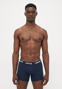 Sötétkék boxer alsónadrág puha anyagból, fehér Levi's logóval a rugalmas derékpánton. Testhezálló kialakítás, látható minták nélkül.