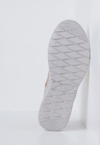 Schuhsohle mit einer strukturierten weißen Gummifläche, die ein Rautenmuster aufweist. Die Seite zeigt ein tanfarbenes Obermaterial mit einem geschwungenen Design für zusätzlichen Komfort.