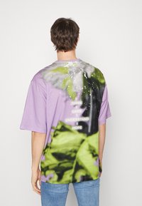 Lila bomull t-shirt med en gradientblommönster och texten "TRO ATT JAG BRYR MIG JAG FÖRSTÅR JAG HOPPAS" på baksidan. Korta ärmar.