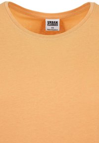 Oranssi puuvillapaita pyöreällä kaula-aukolle. Iholla on ommeltu etiketti, jossa lukee "Urban Classics" ja koko XS. Pehmeä rakenne. Ei kuvioita tai korosteita.