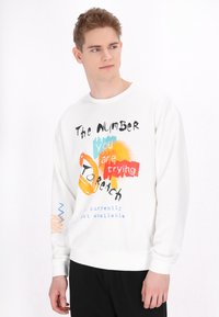 Vit sweatshirt med flerfärgad grafisk text och abstrakta former. L�ångärmade ärmar och ribbade manschetter fulländar designen.