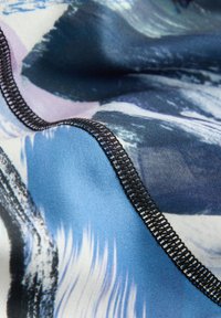 Gros plan d’un tissu à motifs bleu et noir avec une couture en surjet noire le long de la couture courbée.