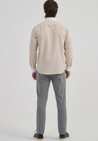 Chemise rayée beige avec col blanc, poignets boutonnés et pantalon gris. Coupe slim, manches longues et rayures verticales discrètes.