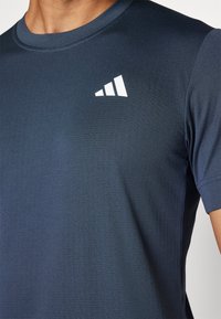 Camiseta atlética de color azul marino, de mangas cortas, hecha de tejido texturizado. Presenta un logo blanco de tres rayas en la parte superior izquierda del pecho.