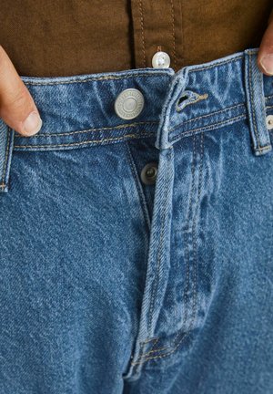 Jeans in denim azzurro con chiusura a bottoni e zip, caratterizzati da una cintura spessa, tasche frontali e dettagli di cucitura visibili.
