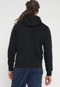 Felpa nera con cappuccio realizzata in un materiale morbido, con vita e polsini aderenti. Presenta un design minimal e una semplice vista posteriore.