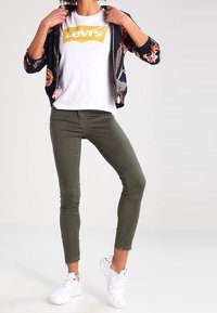 Avslappnad outfit med en bomberjacka i marinblå färg med blommönster, vit t-shirt med Levi's-logotyp, olivgröna jeans och vita sneakers.