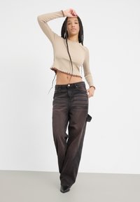 Šviesiai rudas trumpas ilgomis rankovėmis viršus su banguotais kraštais, derinamas su plačiomis juodomis kelnėmis ir smailiais juodais bateliais.