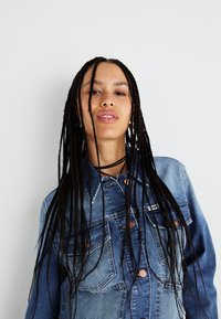 Jasnoniebieska kurtka dżinsowa o klasycznym kroju, z miedzianymi guzikami, podwójnymi kieszeniami na piersi i teksturowanym materiałem.