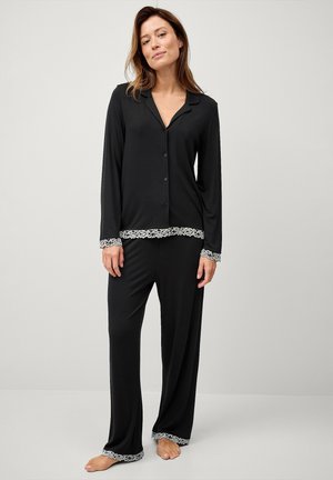 Zwart pyjama set bestaat uit een knoopsluiting top met een kraag en lange mouwen, gecombineerd met losse broek, beide afgewerkt met een kantafwerking.