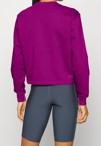 Fioletowy skrócony sweatshirt z okrągłym dekoltem i prążkowanymi ściągaczami, połączony z szarymi szortami rowerowymi o wysokim stanie, z teksturowanej tkaniny.