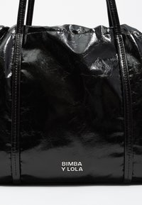 Czarna torebka z lakierowanej skóry o pomarszczonej fakturze, z dwoma uchwytami oraz srebrnym logo "Bimba y Lola" z przodu.