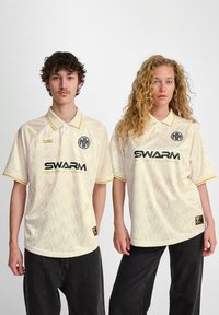 Krämfärgade polo skjortor har gula detaljer, ett subtilt geometriskt mönster och varumärket "SWARM International" på framsidan.