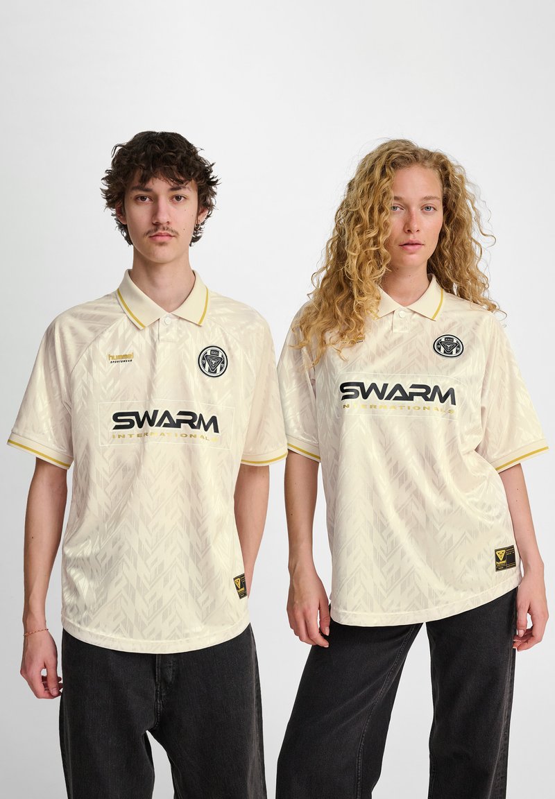 Krämfärgade polo skjortor har gula detaljer, ett subtilt geometriskt mönster och varumärket "SWARM International" på framsidan.