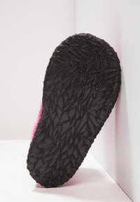 Zwarte rubberen zool met een textuur van een bladerenpatroon, bevestigd aan een roze fluffige bovenkant. De schoen is gepositioneerd tegen een witte achtergrond.