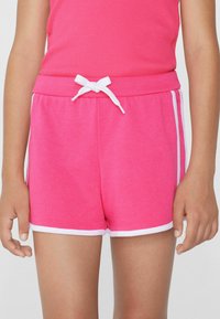 Shorts en coton rose vif avec un cordon blanc et des finitions blanches. Texture douce, coupe décontractée, et rayures latérales qui mettent en valeur le design.