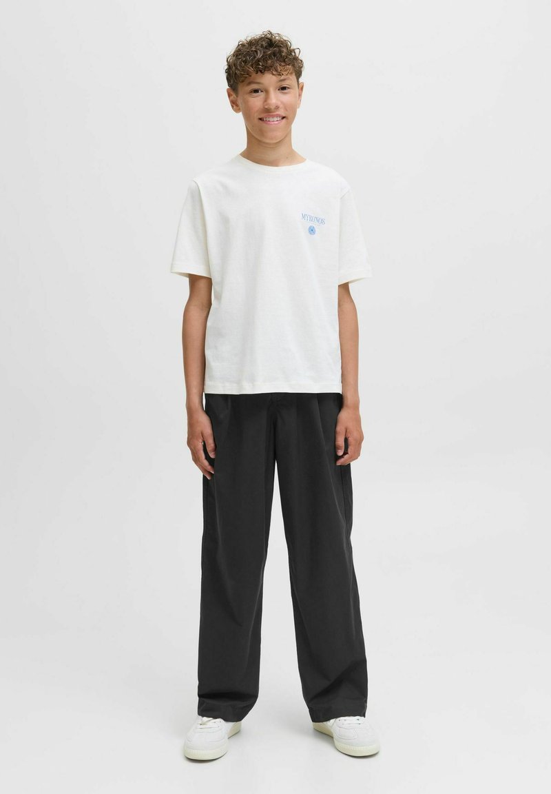 Vit bomulls-t-shirt med korta ärmar och blå tryckt text, tillsammans med löst sittande svarta byxor och vita sneakers.