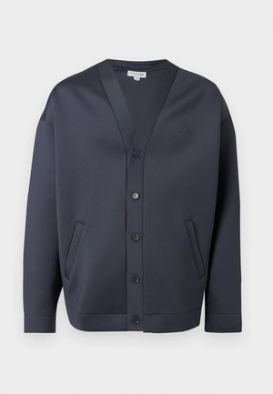 Tmavě námořnická modrá cardigan na knoflíky s výstřihem do V, dvěma bočními kapsami a malým vyšívaným logem na prsou a manžetě rukávu.