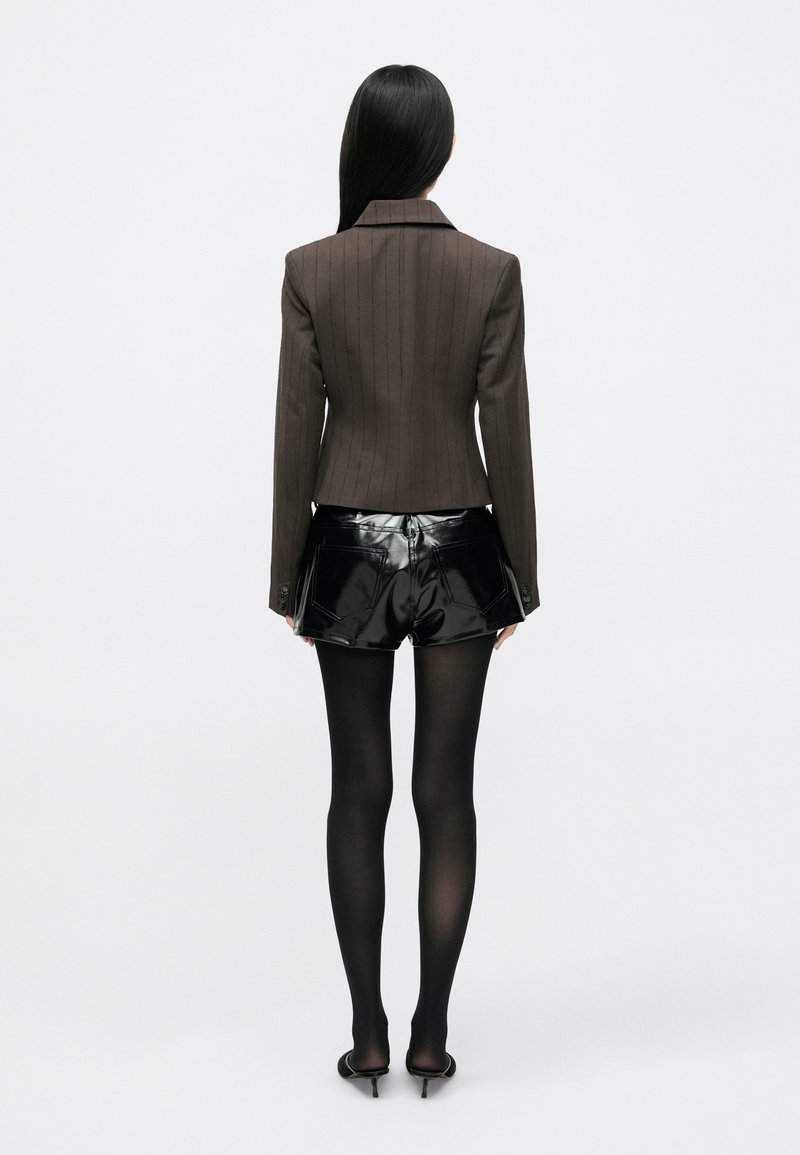 Skræddersyet brun pinstribet blazer med en tætsiddende pasform, parret med skinnende sorte vinylshorts og sorte gennemsigtige strømpebukser, set fra ryggen.