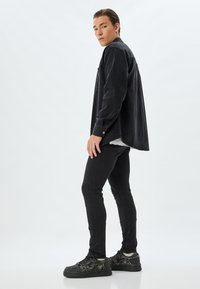 Camisa de mezclilla negra de mangas largas, con un bolsillo lateral, combinada con unos vaqueros negros ajustados y zapatillas negras texturizadas con un diseño estampado.