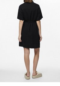 Vestito nero a maniche corte, vita segnata da una cintura. Realizzato in un tessuto testurizzato, presenta un taglio dritto.