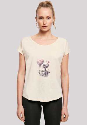 Cream-colored short-sleeve t-shirt featuring a graphic of a skeleton holding a pink heart-shaped balloon and butterflies. Soft, relaxed fit.