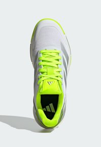 White athletic shoe with a textured mesh upper, bright neon green accents, and laces. Features a logo on the tongue and a cushioned collar.