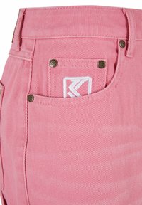 Shorts de mezclilla rosa con textura acanalada diagonal, dotados de remaches metálicos, un bolsillo con parche con bordado blanco y una cinturilla resistente.