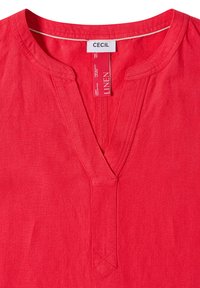 Chemise en lin rouge avec col en V et col étroit, avec étiquette de marque "Cecil" et étiquettes d'entretien du tissu à l'intérieur de l'encolure.