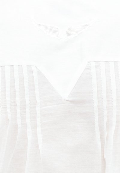 Λευκός γιακάς μπλούζας με δαντέλα και κάθετες πιέτες σε διάφανο ύφασμα κάτω από το ύψος του λαιμού.