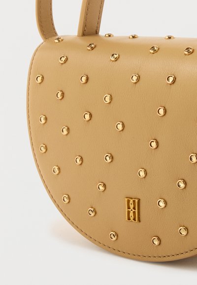 Μπεζ δερμάτινη τσάντα χειρός με διακοσμητικά χρυσά καρφιά και μικρό χρυσό λογότυπο μονόγραμμα στη μπροστινή πτυχή.