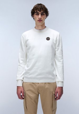 Felpa bianca con maniche lunghe, colletto a costine e una cucitura orizzontale. Presenta un logo rotondo sul petto. Indossata con pantaloni cargo beige.