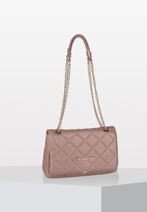 Sac à main matelassé beige Valentino avec rabat, bandoulières chaînes dorées et logo sur le devant, exposé sur un piédestal blanc avec ombre.