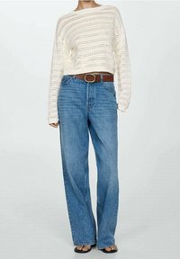 Maglione a maglia beige chiaro con lavorazione aperta, abbinato a jeans a vita alta in denim blu a gamba larga e una cintura marrone con una fibbia rotonda in oro.