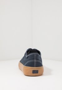 Sneaker in tela marina con cuciture bianche, design a basso profilo, suola in gomma e logo del brand visibile sul tallone.