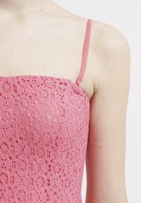 Růžové krajkové šaty s přiléhavou korzetovou částí a jemnými květinovými vzory, s nastavitelnými tenkými ramínky a hladkou texturou.