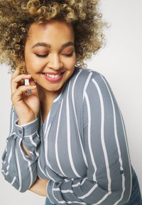 Light blue blouse with white vertical stripes. Features a soft fabric, buttoned cuffs, and a V-neckline.