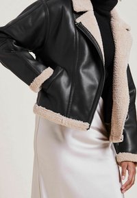 Czarna skórzana kurtka o kroju cropped z beżowym sztucznym futrem podszewkowym i wykończeniem. Posiada zamek błyskawiczny oraz boczne kieszenie.