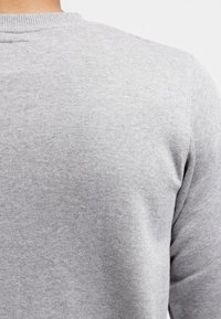 Šedá mikina s jemnou strukturou, kulatým výstřihem a žebrovanými manžetami. Materiál má jemný melírovaný vzor a téměř neviditelné švy.