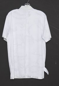 Bílý krátký rukáv Nike Dri-FIT sportovní tričko s jemným maskáčovým vzorem visící na kovovém ramínku na černém pozadí.