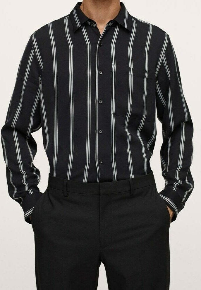 Homme portant une chemise noire à manches longues avec des rayures verticales blanches et un pantalon noir, mains dans les poches, aucun détail visible en arrière-plan.