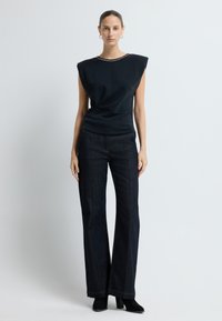 Top nero senza maniche con un design strutturato sulle spalle, colletto decorato; abbinato a jeans a zampa d'elefante in denim scuro a vita alta e stivali neri.