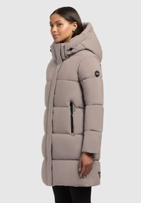 Abrigo tipo puffer en gris claro, con capucha, diseño acolchado, bolsillos laterales con cremallera y detalle del logo en la manga. Presenta un corte recto.