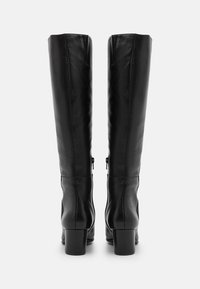 Dobrze dopasowane czarne skórzane kozaki do kolan na słupkowym obcasie, pokazane z tyłu na białym tle.