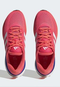 Zapatillas deportivas de color rosa brillante con parte superior de malla, rayas blancas y cordones. Presentan una puntera redondeada y una suela azul en contraste.