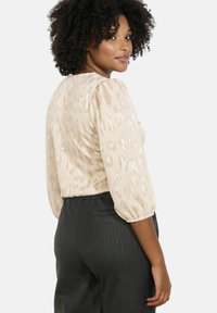 Béžový top s jemným leopardím vzorem, texturovaná tkanina a nafouknuté rukávy, spárovaný s tmavými kalhotami s proužky.