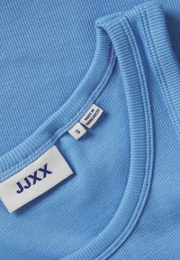 Svetlo modra rebrasta majica brez rokavov s zaobljenim izrezom. Ima oznako z "JJXX," velikost "S," in oznako "Made in Bangladesh."