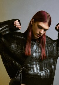 Överdimensionerad svart stickad tröja med vita streck, med en texturerad yta. Svart axelväska hängande över kroppen.